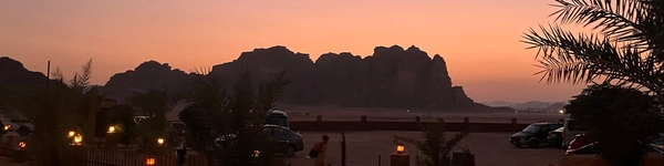 Desert camp at dusk with silhouetted mountains against an orange sky